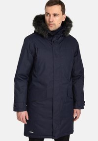 Giacca parka navy con cappuccio in pelliccia sintetica, dotata di chiusura con zip e bottoni, tasche laterali e branding discreto sull'orlo inferiore.