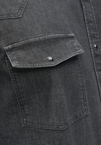 Black denim shirt featuring two chest pockets with snap closures, visible stitching details, and a textured finish. Casual design.