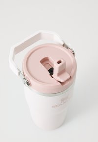 Tasse en acier inoxydable blanc avec un couvercle rose et une poignée blanche, dotée d'une ouverture coulissante et d'un anneau argenté autour du dessus.