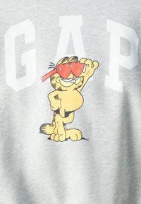 Sudadera gris con un gato de dibujos animados que lleva gafas en forma de corazón. Grandes letras blancas que dicen "GAP" están impresas encima del diseño.