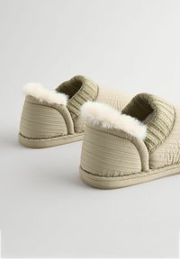 Lys grønne slippers med blød kunstpelskant, ribbet strikket manchet og struktureret stof. Har en polstret sål og stikninger.