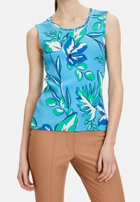 Top sin mangas de tela azul claro con grandes patrones florales en verde y blanco, con cuello redondo y sutiles detalles de costura.