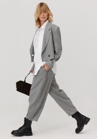 Szara, dopasowana marynarka z usztywnionymi ramionami, biała koszula pod spodem, luźne szare spodnie oraz czarne botki zawiązywane na sznurowadła. Brązowa torebka.