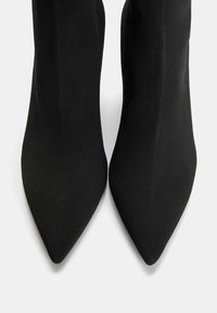 Stivali neri a punta realizzati in un tessuto rigato. Il design presenta una vestibilità aderente, che si estende sopra la caviglia, con una texture liscia.
