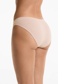 Naadloze nude hipsteronderbroek van een zachte stof, met een lage taille en een minimalistische stijl, die een ronde achterkant benadrukt.