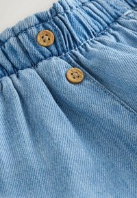Pantaloni din denim albastru deschis cu talie elastică și doi nasturi rotunzi din lemn în fața, în centru.