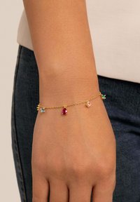 Pulsera de cadena de oro que presenta gemas de colores: una piedra azul, una gota roja y una gema rosa, todas unidas por delicados eslabones.
