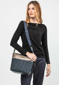 Borsa multicolore con parte superiore metallica e fondo blu testurizzato. Presenta una superficie decorata e una tracolla regolabile con marchio.
