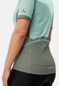 T-shirt de sport à manches courtes en bleu-vert clair avec des accents vert foncé et gris. Présente des panneaux en maille et un logo près de l'ourlet.