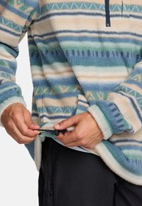 Mikina z fleece s horizontálnymi pruhmi v smotanovej, modrej a zelenej farbe. Má zips na krku a nastaviteľnú šnúrku na spodnom leme.
