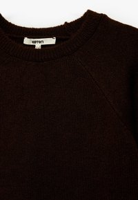 Brązowy sweter dzianinowy z okrągłym dekoltem i raglanowymi rękawami. Tekstura jest miękka, z delikatnym skórzanym wzorem i widoczną metką.