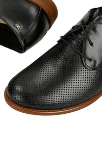 Czarne skórzane buty męskie wizytowe z perforowanymi zdobieniami, brązowymi podeszwami i czarnymi sznurówkami, widoczne z kątem z góry i widoku na piętę.