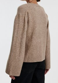 Suéter de lana beige con un corte holgado, cuello redondo y puños y dobladillo acanalados. La textura es suave y ligeramente peluda.
