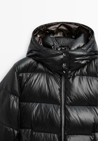 Svart puffjacka med huva, med en glänsande, kviltad design, framsidans dragkedjestängning och tryckknappsdetaljer.