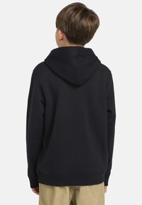 Sudadera negra con capucha, de textura suave, con bolsillo canguro y puños de canalé. La parte trasera presenta un estilo clásico y un diseño sin adornos.