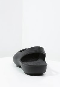 Chaussure noir à enfiler en caoutchouc, dotée d'une forme contour, d'un arrière ouvert et d'une semelle intérieure texturée pour une meilleure adhérence. Fini lisse sans motifs visibles.