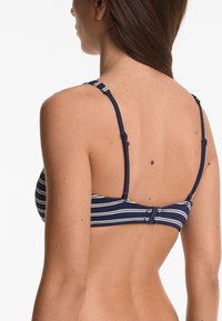 Top bikini a strisce blu navy e bianche con spalline regolabili e chiusura a gancio sul retro, con una texture liscia.