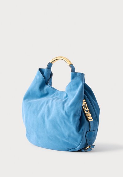Sac à main en daim bleu avec poignée en métal doré et logo doré "MOSCHINO" sur le côté, sur fond clair.