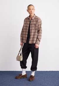 Brown plaid shirt with a chest pocket, black t-shirt, black tapered pants, white socks, brown shoes, and beige crossbody bag.