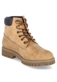 Tan leren boot met een ronde neus, bruine veters, messing oogjes en een zwarte gevoerde kraag. Dikke rubberen zool met een uitgesproken profiel.