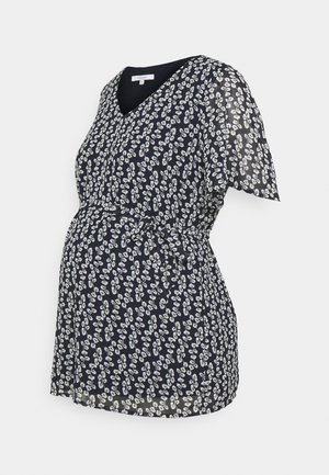 Marineblå graviditetsbluse med hvidt blomstermønster, korte ærmer, V-hals og et bælte i taljen på ensartet baggrund.