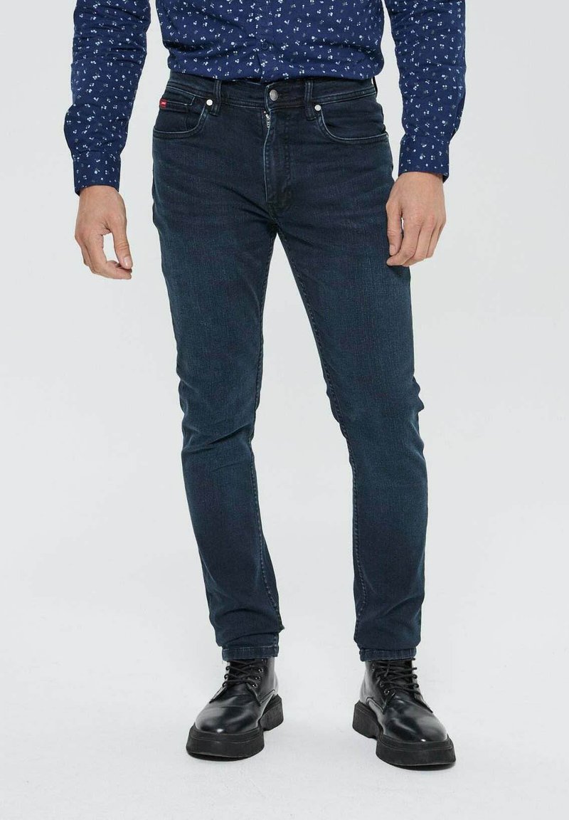 Jean bleu foncé avec une coupe slim, en coton, et une texture subtile. Dispose de cinq poches et d'une fermeture éclair en métal argenté avec un bouton en métal.