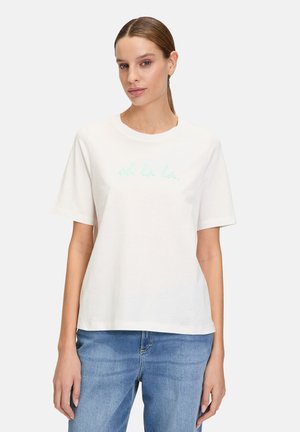 T-shirt en coton blanc à manches courtes, col rond, avec le texte brodé vert clair "oh la la." associé à un jean bleu.