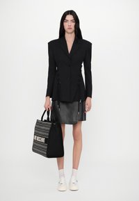 Svart skreddersydd blazer med markerte skuldre, snøring i livet, kombinert med et svart skinnskjørt og en stripete svart tote-veske.