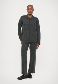 Γκρι πουκάμισο με κουμπιά, δύο τσέπες στο στήθος και διακριτό σχέδιο με κουκίδες, συνδυασμένο με γκρι παντελόνι και ολοκληρωμένο με μαύρες loafers.