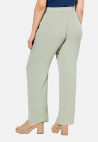 Lichtgroene, wijde broek met een gestructureerde stof en een elastische tailleband, gecombineerd met tankleurige, geweven wedgesandalen.