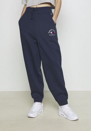 Mørkeblå sweatpants med elastiske manchetter, featuring snoretræk i livet og broderet logo i rød og hvid på venstre lår.