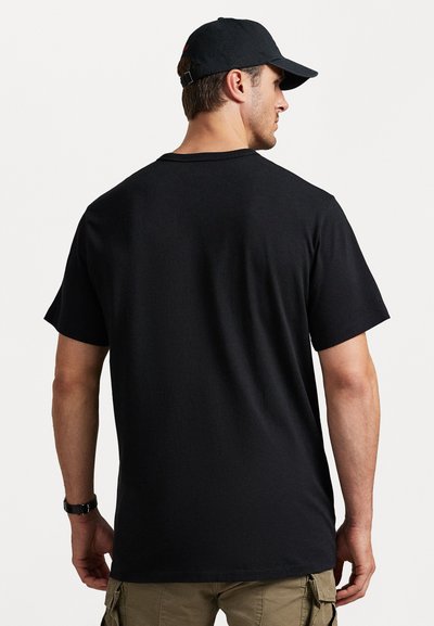 Μαύρο βαμβακερό t-shirt με κοντά μανίκια, στρογγυλή λαιμόκοψη και άνετη εφαρμογή. Φοριέται με μπεζ cargo παντελόνι και μαύρ�ο καπέλο.