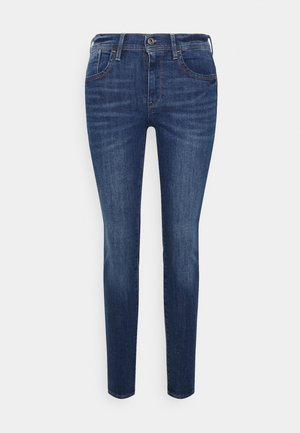 Jean slim bleu foncé avec fermeture devant par boutons et zip, passants pour ceinture et design cinq poches.