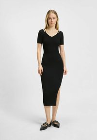 Robe midi noire à côtes avec manches courtes, présentant un décolleté en V et une fente sur le côté. Accentuée par de fines bretelles. Texture lisse.