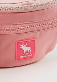 Różowa torba materiałowa o fakturowanej powierzchni, wyposażona w dwa zamki błyskawiczne oraz białą łatę z logo łosia na różowym tle.