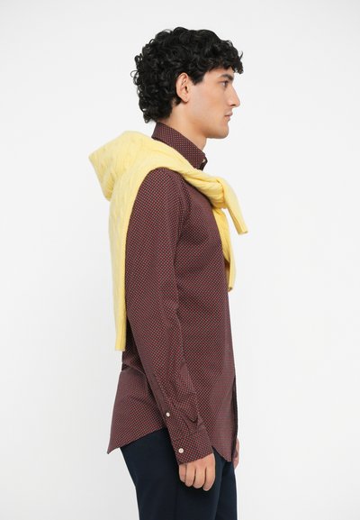 Cămașă cu model roșu, pulover galben din tricot cu cablu aruncat pe umeri, pantaloni bleumarin, textură netedă, croială lejeră, vedere laterală.