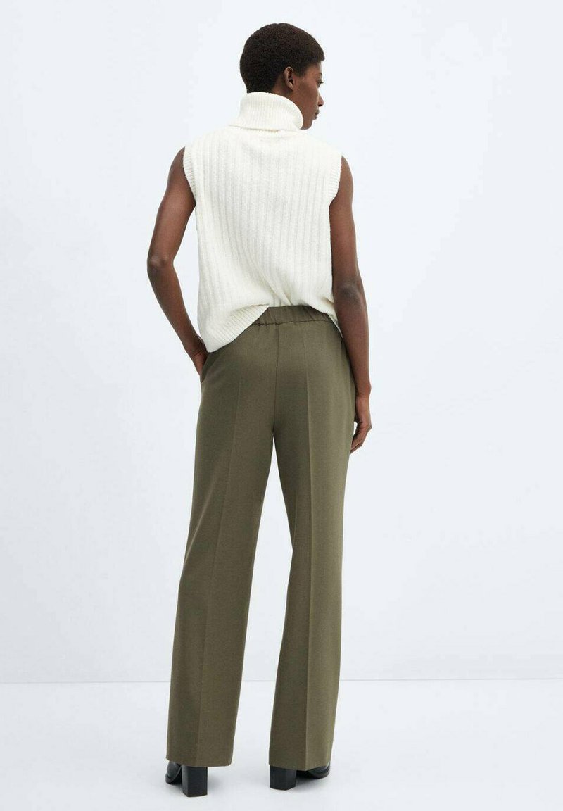 Top bianco a coste senza maniche con colletto alto abbinato a pantaloni larghi a vita alta in verde oliva. L'outfit presenta una vestibilità rilassata e un tessuto lavorato.