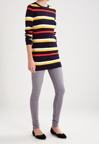 Pull à rayures bleu marine et multicolores à manches longues, associé à un jean skinny gris clair et des chaussures plates noires. Design simple et ajusté.