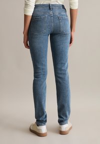 Slim fit niebieskie dżinsy z średnim stanem, tylne kieszenie i subtelne przetarcia, w połączeniu z jasnymi sneakersami.