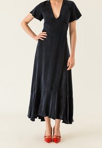 Černé, splývavé maxi šaty s krátkými volánovými rukávy, hlubokým véčkovým výstřihem a volánkovým lemem. Nosené s jasně červenými lodičkami s špičatou špičkou.