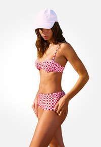 Top de bikini a cuadros rojos y blancos con tirantes ajustables y parte inferior de talle alto a juego, acompañado de una gorra blanca. Textura de tela suave.