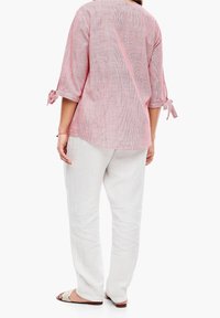 Chemise rayée rouge et blanche à manches longues avec manches retroussées, associée à un pantalon en lin blanc ample. Des sandales simples complètent le look.