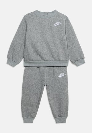 Børne to-delt gråt Nike træningssæt med lange ærmer, elastiske manchetter og hvide Nike-logoer på bryst og venstre lår.