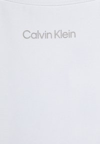 Valge puuvillane T-särk, millel on "Calvin Klein" logo heledates hallides tähtedes. Sile tekstuur ja ümar kaelus.