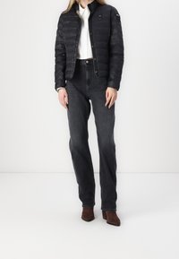 Sort puffertjakke med et tætsiddende design og trykknaplukning. Parret med højalvest mørk denim jeans og brune ankelstøvler med hæl.