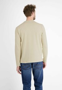 Beige Langarmshirt mit rundem Halsausschnitt, aus weichem Material gefertigt. Getragen mit blauen Jeans, die eine lässige Passform und Standarddetails zeigen.