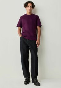 Paarse t-shirt met korte mouwen, gecombineerd met donkerdenim broek en zwarte veterschoenen. Eenvoudig ontwerp met een ronde hals en een ontspannen pasvorm.