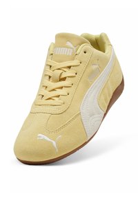Baskets Puma en suède jaune avec logo blanc, lacets à l'avant, bande latérale blanche et semelle en caoutchouc marron, inclinées pour montrer l'avant et le côté.