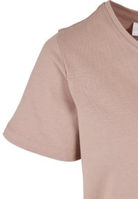 T-shirt en coton rose clair avec un col en V et des manches courtes. Présente une texture lisse et des coutures propres le long des bords des manches.