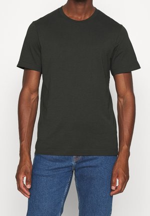 Man wearing a plain black short-sleeve crew neck t-shirt and blue jeans standing with arms relaxed at sides.